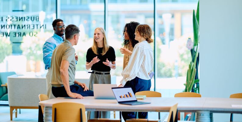 Colleagues gathered around a table in a modern office workspace, representing IM Group’s evolving approach to workplace management with Resource Central.
